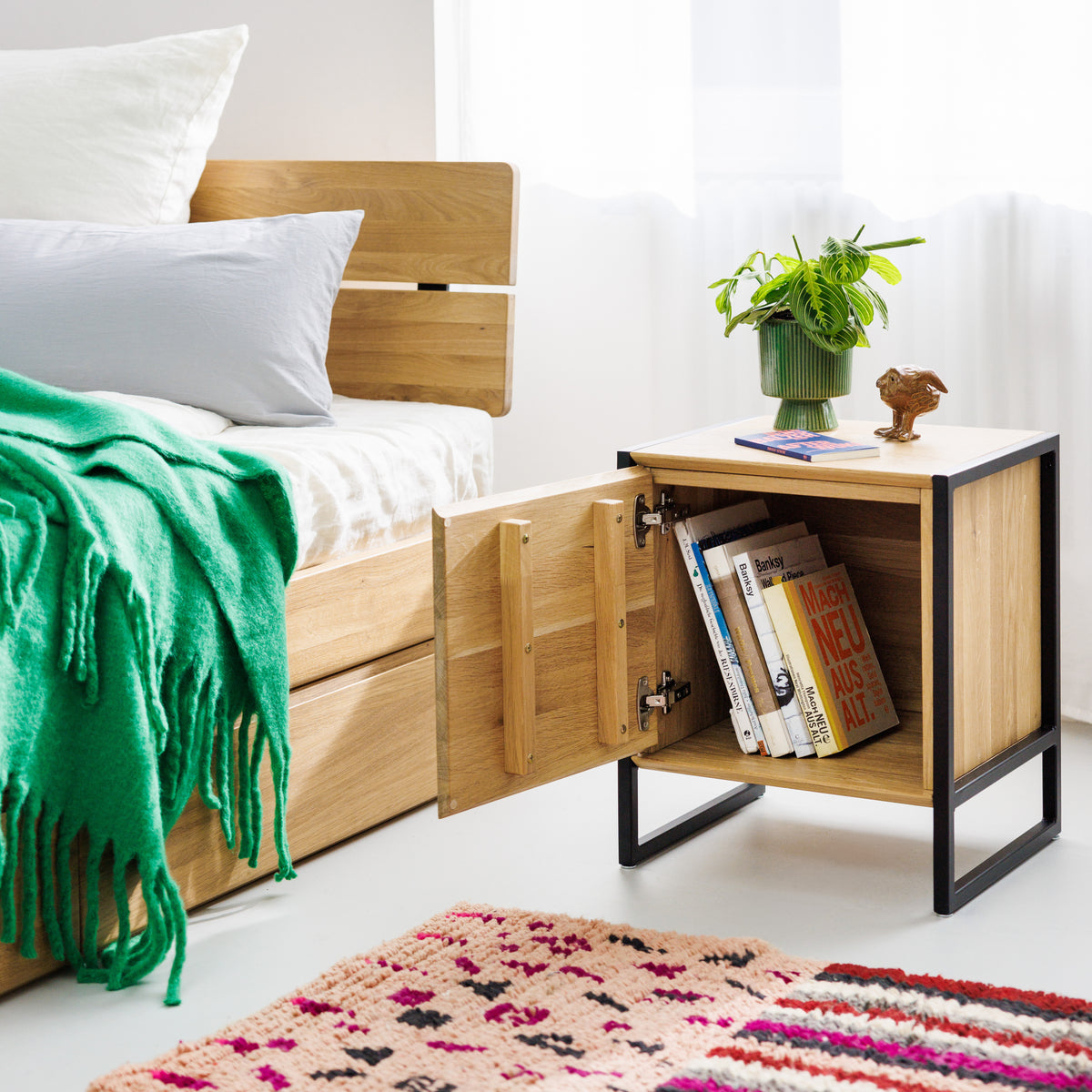 Nachttisch mit Tür aus Massivholz neben Designerbett aus Eiche mit schwarzen Metallelementen